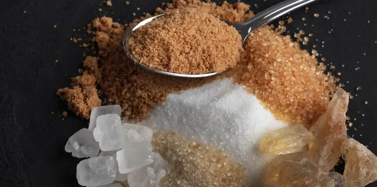 Buy jaggery powder online in India: A silver spoon filled with fine, natural brown jaggery powder placed over a variety of traditional Indian sweeteners like palm candy and raw cane sugar.