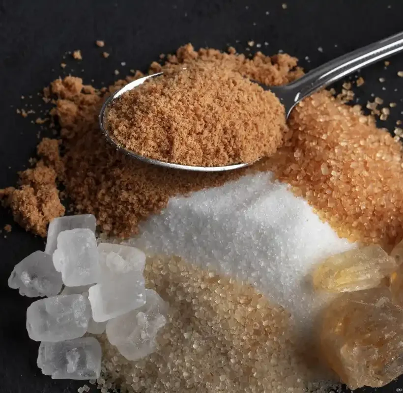 Buy jaggery powder online in India: A silver spoon filled with fine, natural brown jaggery powder placed over a variety of traditional Indian sweeteners like palm candy and raw cane sugar.